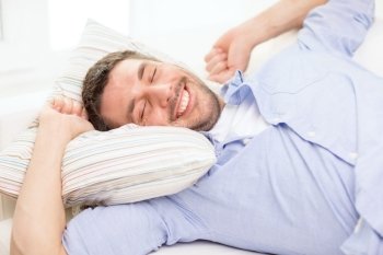 home and happiness concept - smiling young man lying on sofa at home