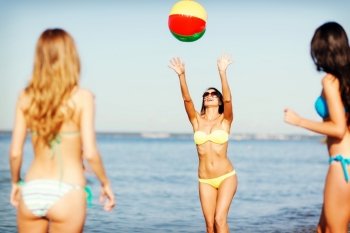 summer holidays, vacation and beach activities concept - girls in bikinies playing ball on the beach