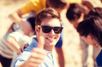 summer, holidays, vacation, happy people concept - man with group of friends on the beach showing thumbs up