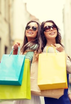 shopping, sale, happy people and tourism concept - two smiling girls in sunglasses with shopping bags in ctiy