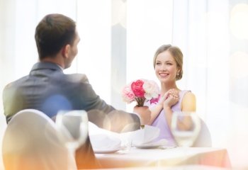 restaurant, couple and holiday concept - smiling woman recieving bouquet of flowers from husband or boyfriend at restaurant