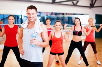 fitness, sport, training, gym and lifestyle concept - smiling trainer in front of group of people working out with barbells in the gym