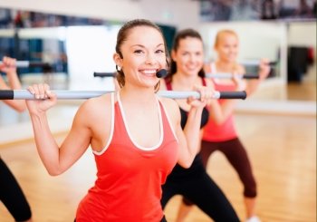 fitness, sport, training, gym and lifestyle concept - smiling trainer in front of the group of people working out with barbells in the gym