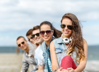 summer holidays and teenage concept - smiling teenage girl in sunglasses hanging out with friends outdoors