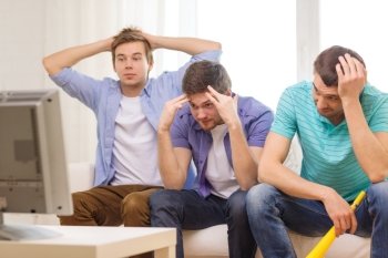 friendship, sports and entertainment concept - sad male friends with vuvuzela watching sports on tv at home