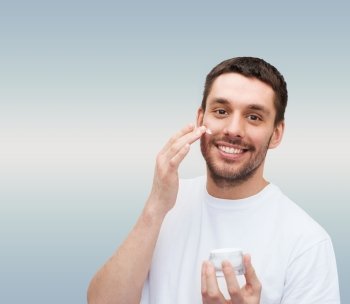 health and beauty concept - beautiful smiling man with jar of cream applying cream