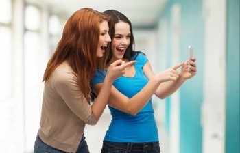 technology, friendship and people concept - two smiling teenagers pointing finger at smartphone