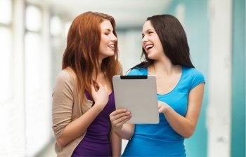 technology, friendship and people concept - two smiling teenagers pointing finger at tablet pc screen and looking at each other