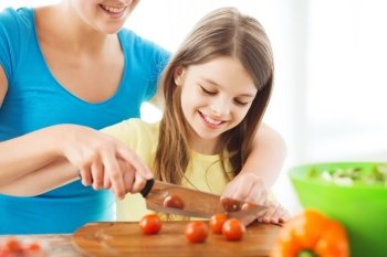 family, child, cooking and home concept - smiling little girl with mother chopping tomatoes in the kitchen