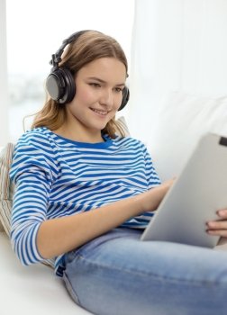 home, music, technology and internet concept - smiling teenage girl lying on the couch with tablet pc computer and headphones at home