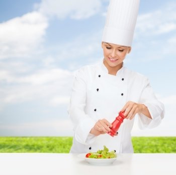 cooking and food concept - smiling female chef preparing salad with salt or pepper mill