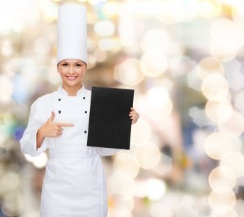 cooking, advertisement and food concept - smiling female chef pointing finger to blank black paper