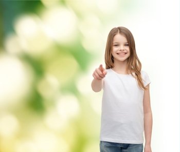 gestures and happy people concept - happy little girl in blank white t-shirt pointing at you