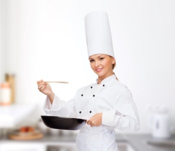 cooking and food concept - smiling female chef with pan and spoon tasting food
