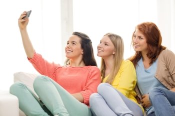 friendship, technology and internet concept - three smiling teenage girls taking selfie with smartphone camera at home