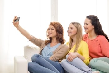 friendship, technology and internet concept - three smiling teenage girls taking selfie with smartphone camera at home
