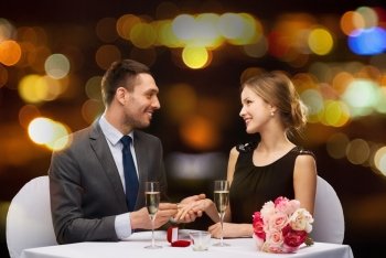 restaurant, couple and holiday concept - smiling man putting on finger engagement ring at restaurant