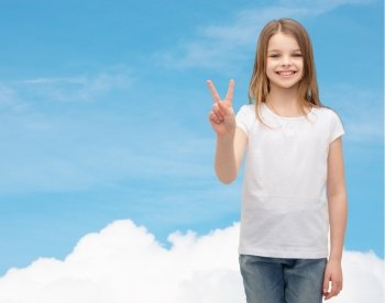 gesture and happy people concept - smiling little girl in white blank t-shirt showing peace gesture with fingers