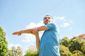 fitness, sport, training and lifestyle concept - smiling man stretching hand outdoors