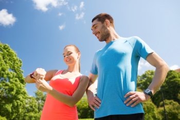 fitness, sport, training, technology and lifestyle concept - two smiling people with heart rate watches outdoors