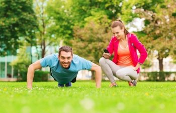 fitness, sport, training, technology and lifestyle concept - smiling man with personal trainer doing exercise outdoors