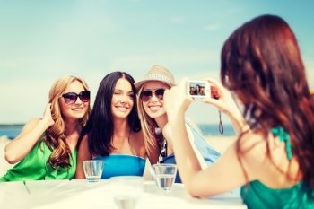 summer holidays and vacation - girls taking photo with digital camera in cafe on the beach
