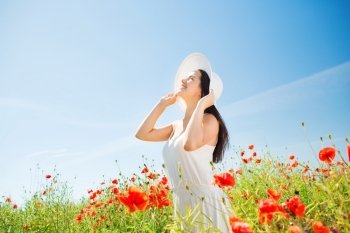 happiness, nature, summer, vacation and people concept - smiling young woman wearing straw hat looking up on poppy field