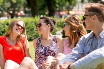 friendship, leisure, summer and people concept - group of smiling friends outdoors sitting on grass in park