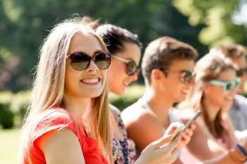 friendship, leisure, summer, technology and people concept - group of smiling friends with smartphones sitting in park
