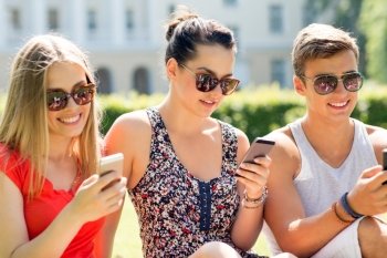 friendship, leisure, summer, technology and people concept - group of smiling friends with smartphones sitting on grass in park