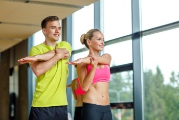 sport, fitness, lifestyle and people concept - smiling man and woman stretching in gym