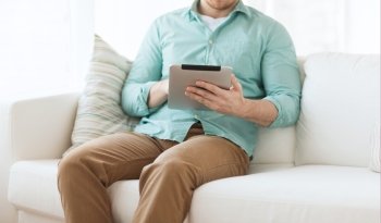technology, leisure, lifestyle and distance learning concept - close up of man working with tablet pc computer sitting on sofa at home