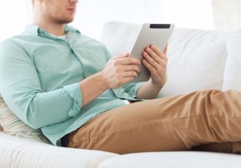 technology, leisure, lifestyle and distance learning concept - close up of man working with tablet pc computer sitting or lying on sofa at home