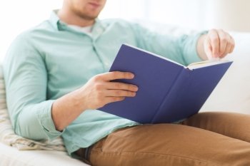 leisure, education, literature and home concept - close up of man and sitting or lying on couch and reading book at home