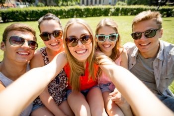 friendship, leisure, summer, technology and people concept - group of smiling friends making selfie with smartphone camera or tablet pc in park