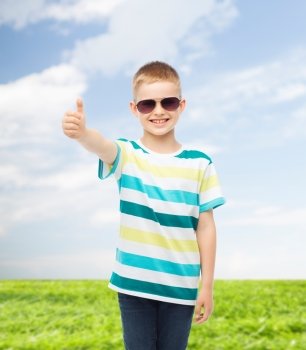 happiness, summer, childhood, gesture and people concept - smiling cute little boy in sunglasses over natural background showing thumbs up