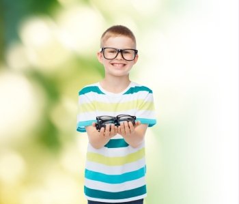 vision, health, ecology and people concept - smiling little boy in eyeglasses holding spectacles over green background