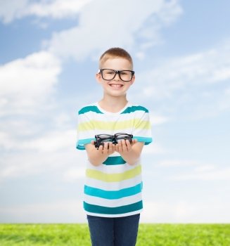 vision, health, childhood and people concept - smiling little boy in eyeglasses holding spectacles natural background
