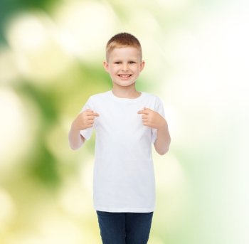 advertising, ecology, gesture and childhood concept - smiling boy in white blank t-shirt pointing fingers at himself over green background