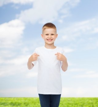 advertising, people and childhood concept - smiling little boy in white blank t-shirt pointing fingers at himself over natural background
