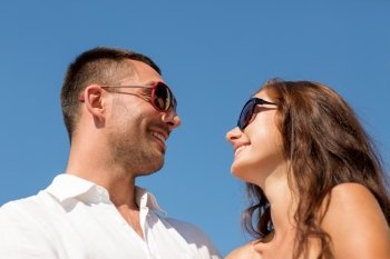 love, travel, tourism, people and friendship concept - smiling couple wearing sunglasses looking at each over blue sky background