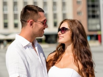 love, travel, tourism, people and friendship concept - smiling couple wearing sunglasses looking at each other in city