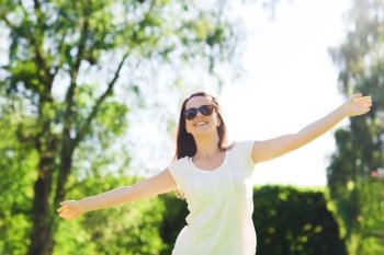 summer, leisure, vacation and people concept - smiling young woman wearing sunglasses standing in park