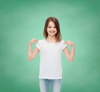 advertising, gesture, education, childhood and people - smiling girl in white t-shirt pointing fingers on herself over green board background