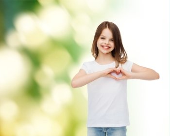 advertising, childhood, ecology, charity and people - smiling little girl in white t-shirt making heart-shape gesture over green background