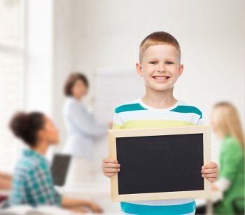 education, school, advertisement, teamwork and people concept - smiling little boy holding blank black chalkboard over background