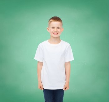 happiness, childhood, school education, advertisement and people concept - smiling little boy in white t-shirt over green board background