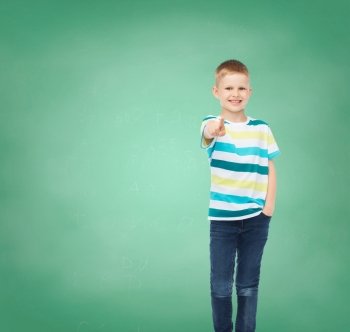 happiness, school, education, gesture and people concept - smiling boy pointing his finger at you over green board background
