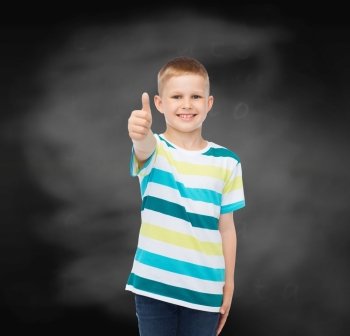 happiness, childhood, school, education and people concept - smiling little boy showing thumbs up over blackboard background