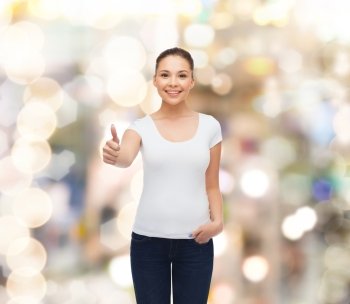 advertising, holidays, gesture and people concept - smiling young woman in blank white t-shirt showing thumbs up over sparkling background